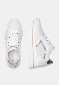Baskets de sport blanches avec une tige en mesh, des accents métalliques et un panneau latéral texturé. Présente du matériel en ton or et une semelle rembourrée.
