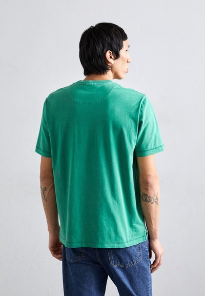 Πράσινο βαμβακερό μπλουζάκι με κοντά μανίκια, στρογγυλή λαιμόκοψη και χαλαρή εφαρμογή. Διαθέτει ραμμένες λεπτομέρειες και ανοίγματα στο πλάι.