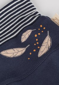 Tessuto blu navy con tre stampe di piume beige e macchie arancioni sparse accanto a un tessuto a righe bianche e nere.