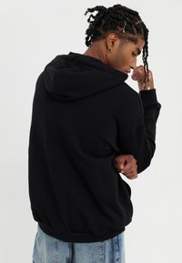 Black hooded sweatshirt with a relaxed fit, featuring ribbed cuffs and hem, worn with faded blue denim jeans.