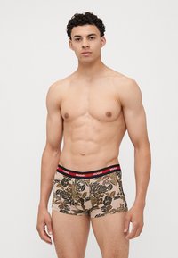Boxer-briefs pour hommes avec un motif floral beige et des feuilles vertes et brunes, ceinture noire avec le logo rouge "HUGO", en mélange de coton.