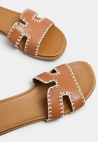 Brązowe skórzane klapki z dwoma szerokimi paskami z białymi przeszyciami, płaską podeszwą i okrągłym przodem.