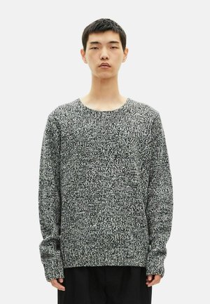 Sweatshirt en tricot noir et blanc, doté d'un col rond et de manches longues avec des poignets côtelés, mettant en avant un motif texturé.