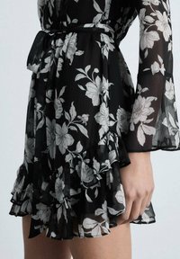 Black floral dress featuring sheer fabric, white flower print, long bell sleeves, ruffled hem, and a fabric belt at the waist.