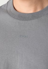 Grijze ronde hals t-shirt van zachte katoen met een zichtbaar reliëf "HUGO" logo op de borst. Gladde textuur en aansluitend ontwerp.