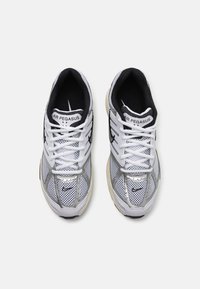 Baskets en maille blanches avec des accents noirs, des détails en argent et une semelle texturée. Comprend des lacets et une branding sur la languette.