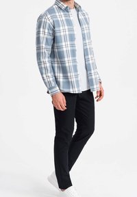 Camisa de cuadros azul y blanca con cuello, llevada sobre una camiseta blanca. Combinada con pantalones ajustados negros y zapatillas blancas.