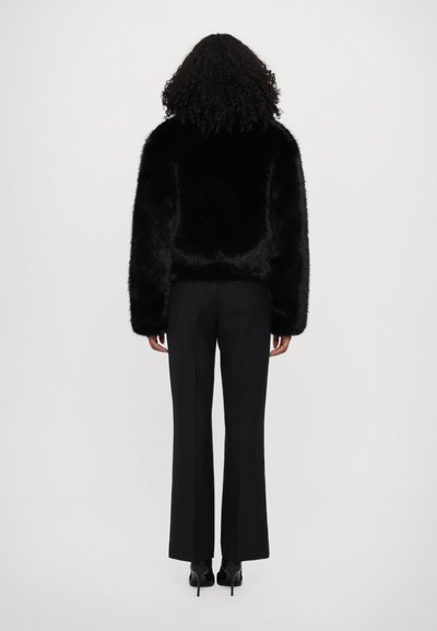 Giacca cropped in pelliccia sintetica nera con maniche lunghe e vestibilità comoda, abbinata a pantaloni neri su misura e scarpe con tacco alto.