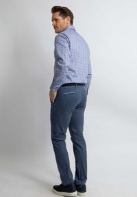 Herenblauw geruit overhemd met button-down kraag, gecombineerd met donkerblauwe broek en zwarte sneakers. Glad materiaal, slim fit ontwerp.