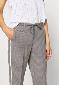 Szare i czarne spódnie w kratę z elastycznym pasem na sznurki, bocznymi kieszeniami i białym paskiem kontrastowym wzdłuż zewnętrznego szwu.