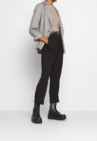 Šedý kostkovaný blazer, béžový svetr, černé kalhoty s vysokým pasem a černé šněrovací boty s tlustou podrážkou. Obsahuje opasek s cvočky.