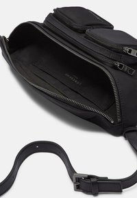 Borsa nera in nylon con una superficie liscia, dotata di due scomparti con zip, un ampio interno e una tracolla in pelle. I dettagli della zip sono visibili.