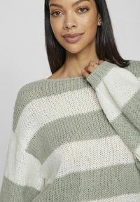 Übergroßer Strickpullover mit abwechselnd grünen und weißen Streifen, aus einem weichen, strukturierten Stoff gefertigt, mit weitem Bootsausschnitt und gerippten Bündchen.