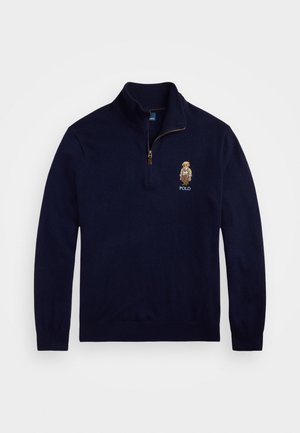 Marinblå pullovertröja med krage som kan dra i en fjärdedel, tillverkad av mjukt tyg. Har en broderad logotyp och en detaljerad karaktärsdesign.