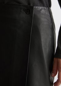 Sorte læderskørt med en glat tekstur, der har en sideslids og en rund sort knap i taljen. Skræddersyet design med rene linjer.