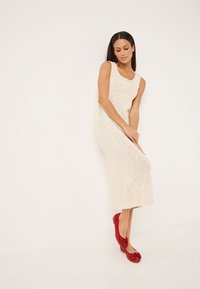 Vestido de punto crema hasta la rodilla con escote en forma de barco y patrón texturizado, combinado con unos zapatos planos rojos con detalle de lazo.