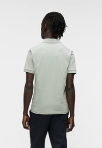 Μπλούζα πόλο σε ανοιχτό πράσινο βαμβάκι με κοντά μανίκια και γιακά, φορεμένη με σκούρο παντελόνι, που παρουσιάζει έναν απλό και μινιμαλιστικό σχεδιασμό.