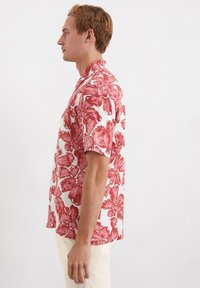 Korte mouw blouse met een witte basis en gedurfde rode bloemenpatronen. Gemaakt van lichtgewicht materiaal met een losse pasvorm en kraagontwerp.