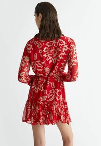 Red floral dress with long sheer sleeves, tie waist, and ruffled hem, featuring white floral patterns throughout.