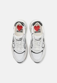 Hvite sneakers med svarte aksenter, med en perforert tåboks og "LOVE MOSCHINO" merking. Rød hjertegrafikk på innersålene. Teksturert såle.
