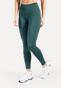 Legginsy w kolorze morskim o wysokim stanie, wykonane z elastycznego materiału, cechujące się gładką teksturą i dopasowanym krojem. Połączone z białymi sportowymi trampkami.