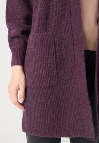 Purple knit cardigan with ribbed texture, open front, and side pockets. Material appears soft and warm, with a relaxed fit.