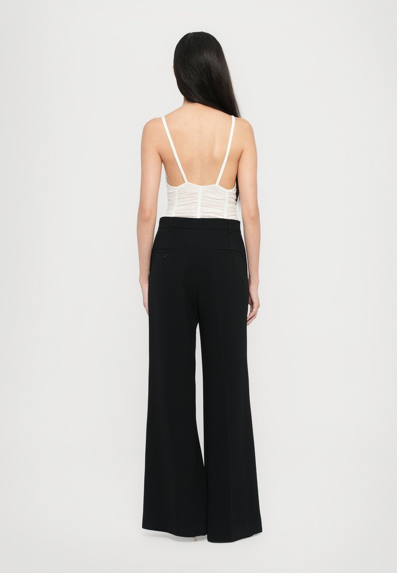 Top bianco aderente con spalline sottili e design texturizzato, abbinato a pantaloni neri a vita alta e gamba larga con tasche sul retro.