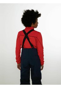 Camicia rossa a maniche lunghe con colletto alto, abbinata a pantaloni da sci blu scuro. Cinghie nere si incrociano sul retro. Texture liscia, design funzionale.