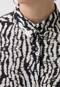 Camicia a righe bianco e nero con colletto, che mostra un tessuto strutturato e bottoni circolari lungo la parte anteriore.