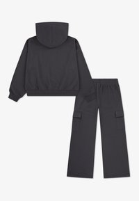 Σκούρο γκρι, κομμένο φούτερ με κουκούλα και μακριά μανίκια, σε συνδυασμό με παντελόνια φαρδιάς γραμμής που διαθέτουν πλαϊνές τσέπες cargo. Μαλακή υφή υφάσματος.