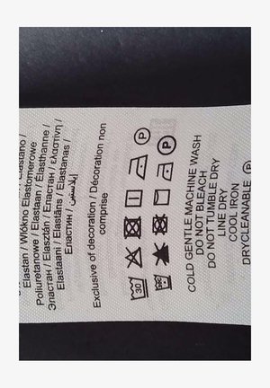 Metka z instrukcjami prania, w dominującej białej kolorystyce, z czarnym tekstem oraz symbolami do prania, suszenia i prasowania.