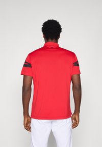 Červená atletická poloko�šeľa s golierom, so čiernymi pruhmi na ramenách. Hladká tkanina, krátke rukávy a voľný strih.