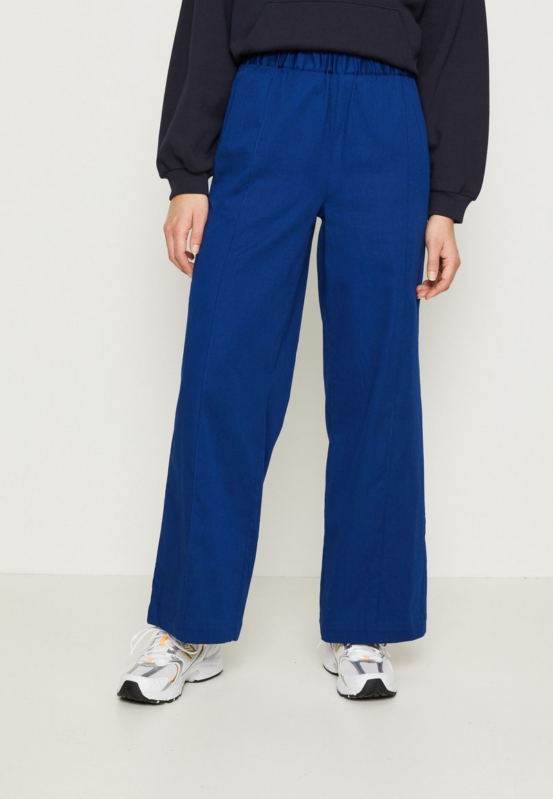 Modré kalhoty s širokými nohavicemi a elastickým pasem, vyrobené z hladké látky, s volným střihem a minimem švů.