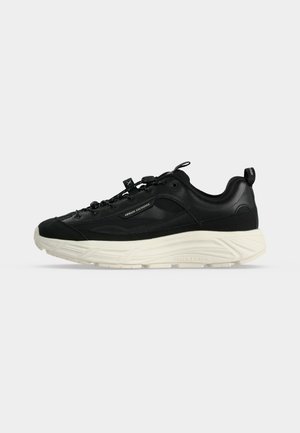 Czarny niski sneaker z grubą białą podeszwą, oznaczony marką "Armani Exchange" z boku i na podeszwie, wyposażony w pętlę do ściągania i zapięcie na troczki.
