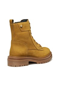 Botas de tobillo de cuero amarillas con punta redondeada, suela de goma y ojales de metal. Cuenta con una solapa lateral con un botón de presión.