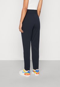 Pantalons fuselés bleu marine avec une taille haute, en tissu doux ; portés avec des baskets colorées présentant de multiples accents.