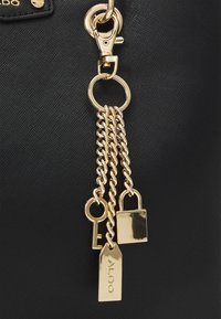 Sort tekstureret materiale taske med et guldfarvet metal kædeaccent og vedhæftede detaljer som nøgle, lås og tag.
