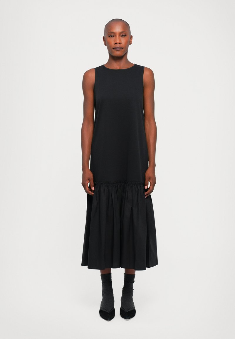Schwarzes ärmelloses Kleid mit einem figurbetonten Oberteil und einem gerafften, knie-langen Rock. Hergestellt aus glattem Stoff und mit einem einfachen, minimalistischen Design.