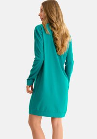 Teal langemouwen jurk in een losse pasvorm, met een ronde zoom en zachte stof. De achterkant toont een soepele silhouet.