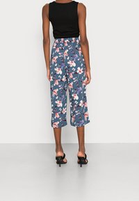 Blommiga culottebyxor i blått med rosa och lila blommor, elastisk midja och kapad längd, tillsammans med en svart ärmlös topp.