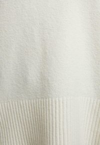 Light cream sweater featuring a textured top section and a ribbed lower hem. Soft, cozy knit material with subtle variations in tone.