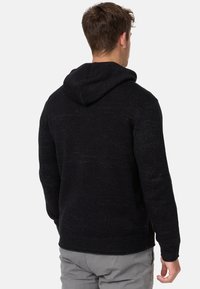 Schwarzer Strick-Hoodie mit strukturiertem Muster, ausgestattet mit einer Kordelzugkapuze sowie gerippten Bündchen und Saum, von hinten gezeigt.