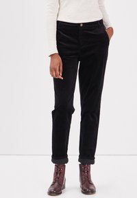 Svarta kordflorbyxor med rak benpassform, med framfickor och uppvikta muddar, tillsammans med bruna snörstövlar vid anklarna.