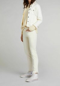 Valkoinen farkkutakki hopeisilla napeilla, kermaisen värinen neulepusero ja valkoiset kapealahkeiset farkut yhdistettyinä valkoisiin kangaskorkeavartisiin lenkkareihin.