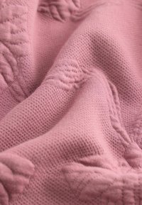 Tessuto rosa testurizzato con un motivo intrecciato, caratterizzato da design floreali in rilievo e una texture morbida, leggermente elasticizzata.