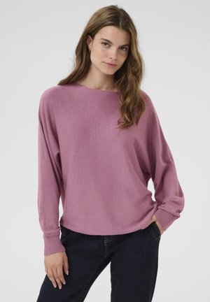 Hellrosa, übergroßer Pullover mit langen Ärmeln und gerippten Bündchen, aus einem weichen, strukturierten Material, kombiniert mit dunklen Jeans.