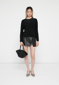 Pull noir en tricot avec des embellissements au niveau du col, associé à une mini-jupe en cuir noir et un sac à main structuré noir. Chaussures à petit talon.