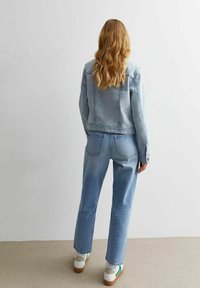 Vaaleansininen farkkutakki, jossa on hieman lyhennetty malli, yhdistettynä korkeavyötäröisiin vaaleansinisiin farkkuihin. Molemmissa on klassinen istuvuus ja hienovarainen tekstuuri.