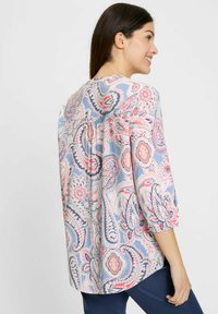 Blusa azzurro chiaro con motivi paisley in rosa, rosso e blu scuro. Maniche a tre quarti con dettagli arricciati nella parte posteriore. Tessuto morbido al tatto.