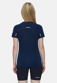 Marinblå kortärmad träningsskjorta i texturerad tyg, med en logotyp på baksidan. Parats med mörka shorts, designade för aktivitet.